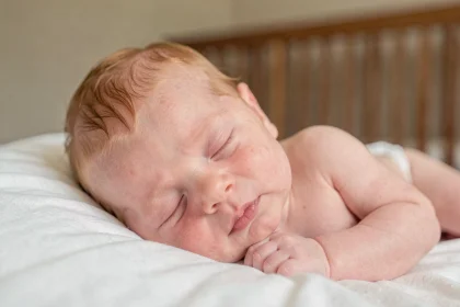 Nouveau-né roux aux traits délicats endormi sur une couverture blanche, phototype clair avec peau translucide rosée